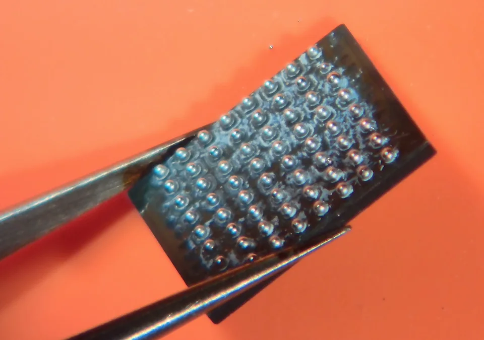 A BGA64 chip held with tweezers, showing the solder-ball array on its underside.